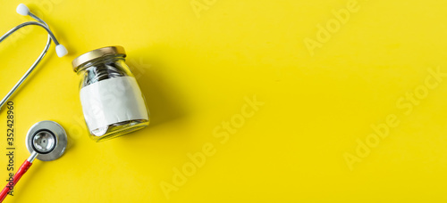 Banner of Savings and insurance concepts. Coins in a bottle with doctor headphones or red stethoscope. Saving for life insurance,retirement,health on the yellow background copy space.