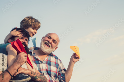 Men generation. Happy child playing with toy paper airplane against summer sky background. Cute son with dad playing outdoor. Happy family. Father and son with grandfather - happy loving family.