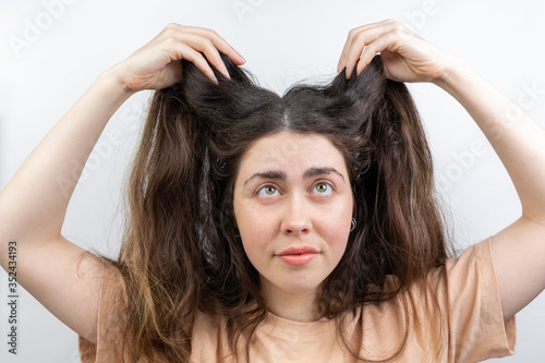 Dandruff, pediculosis and seborrhea. Portrait of a young Caucasian woman, a brunette, who lifts her hair with her hand, looking up. White background