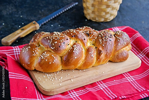 Homemade challah, traditional wicker white bread on a wooden board on a black concrete background. Copyspace photo