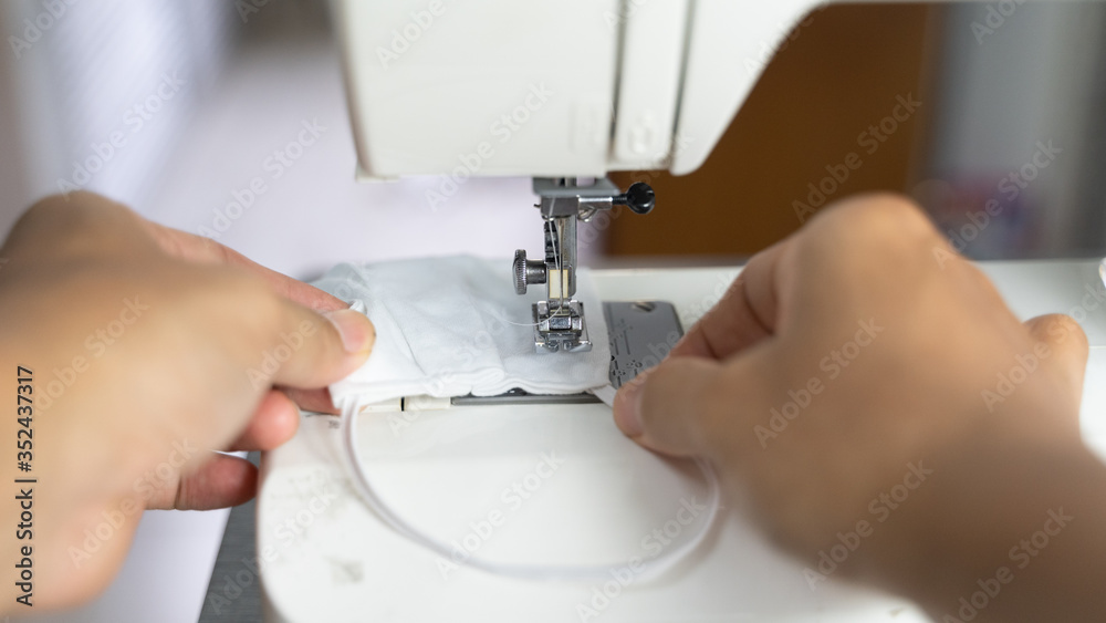 Electric sewing machine with fabric and thread, defocus hand hold on protective mask , antivirus  face mask during a pandemic virus COVID-19