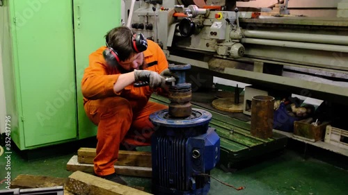 NatIg Aliev tanker skilled worker in bright orange costume with headphones on head repairs electric motor on deck closeup photo