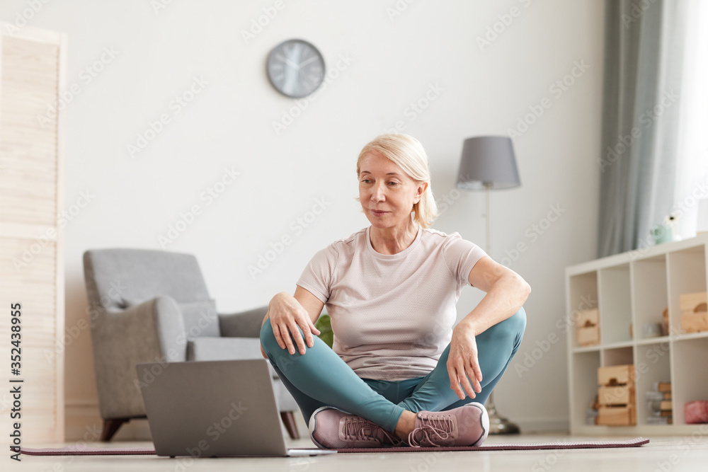 Senior woman sitting on the floor and looking at monitor of laptop she preparing for the sport exercises Senior woman sitting on the floor and looking at monitor of laptop she preparing for the sport exercises