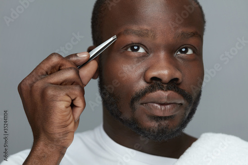 Male Eyebrow Grooming. Closeup Of Model Removing Brow Hair With Tweezers. Facial Hair Plucking As Beauty Concept.