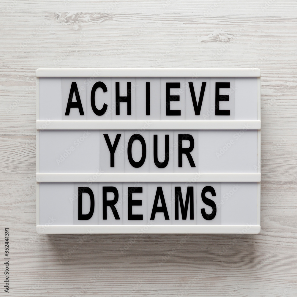 'Achieve your dreams' words on a lightbox on a white wooden background, top view. Overhead, from above, flat lay. 'Achieve your dreams' words on a lightbox on a white wooden background, top view. Overhead, from above, flat lay.