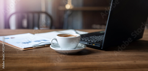 Cropped shot place of work on wooden table have coffee drink, laptop, paperwork of investment, Concept work from home