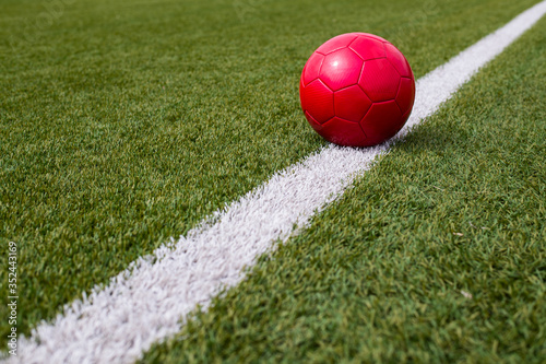 a red soccer ball is lying on a green soccer field next to the line