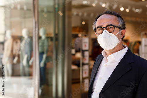 uomo con occhiali neri vestito elegante  e con mascherina facciale Kn95 davanti a un negozio nelle vie del centro photo