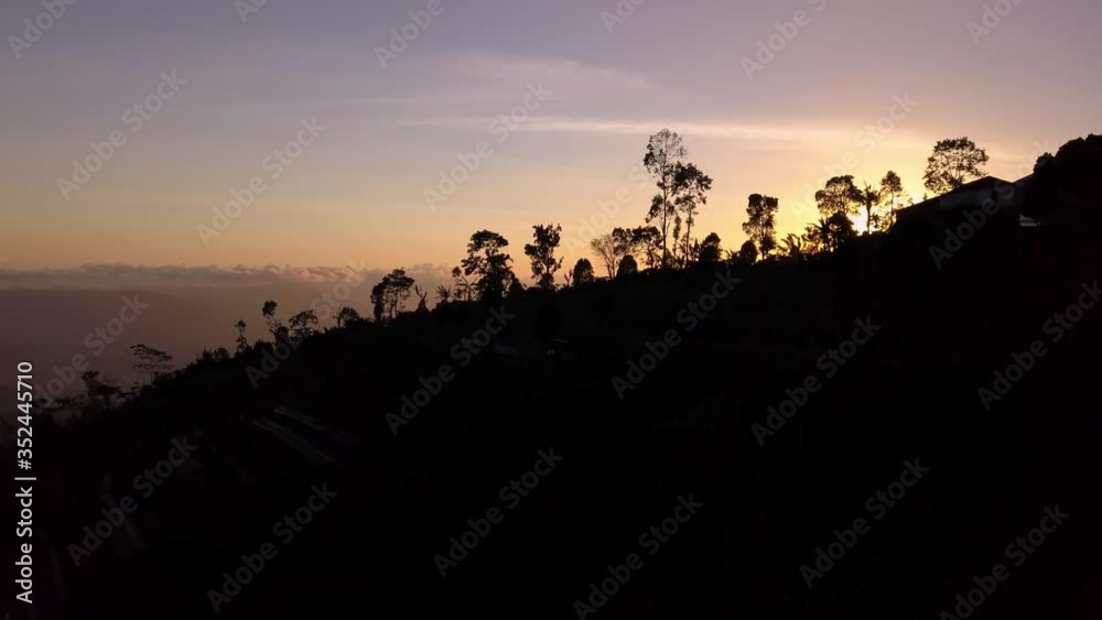Ocean Sunset in Bali Indonesia from mountain top with trees in silhouette, Aerial pedestal lift reveal shot Ocean Sunset in Bali Indonesia from mountain top with trees in silhouette, Aerial pedestal lift reveal shot