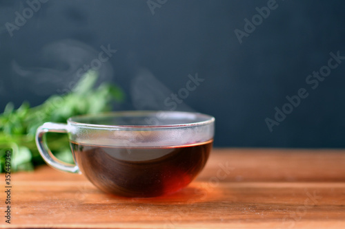 Hot black tea in a transparent glass cup on a wooden table and mint background