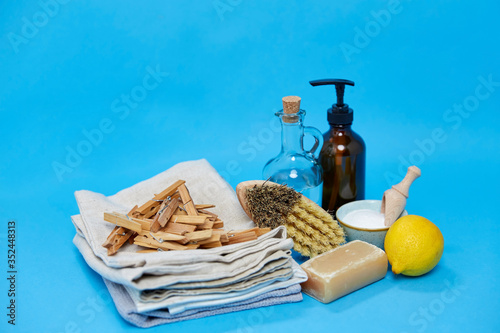 natural cleaning stuff and eco living concept - washing soda, lemon, bottle of vinegar, liquid soap and brush with wooden clothespins on canvas towels over blue background