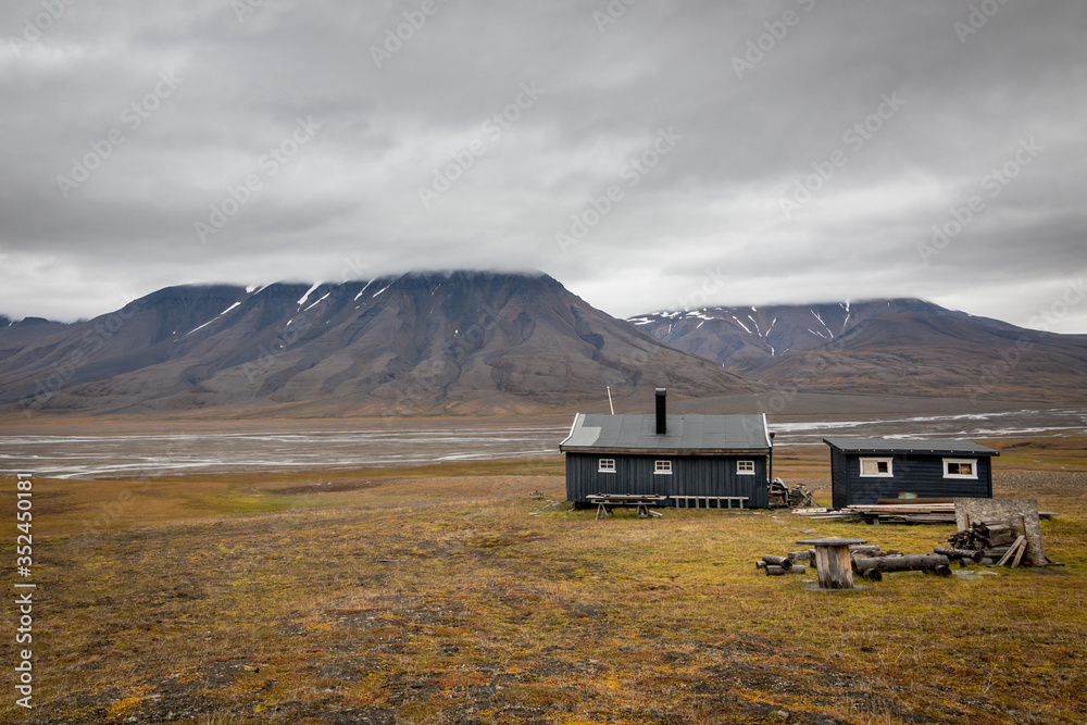 Typical wooden cottage in the arctic landscape in Svalbard, Norway. Scenic view of Adventdalen (Advent valley) in August when autumn starts, lichen and grass turn orange 