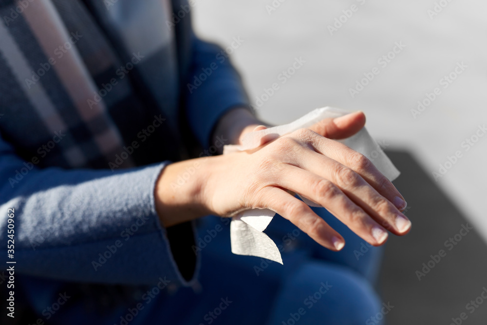 hygiene, health care and safety concept - close up of woman cleaning hands with antiseptic wet wipe outdoors