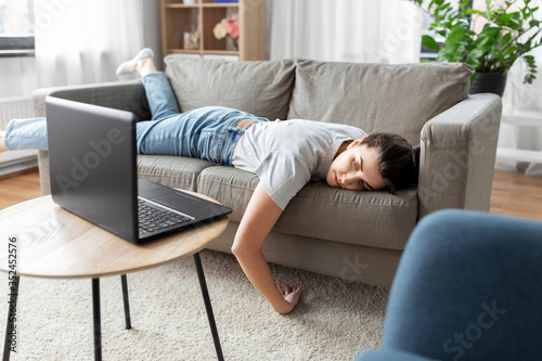 people, boredom and depression concept - bored or lazy young woman with laptop computer lying on sofa at home photo