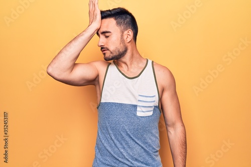 Young handsome man with beard wearing sleeveless t-shirt standing over yellow background surprised with hand on head for mistake, remember error. Forgot, bad memory concept. © Krakenimages.com
