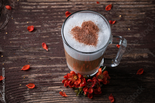 A glass with latte macchiato on wooden background with red flowers