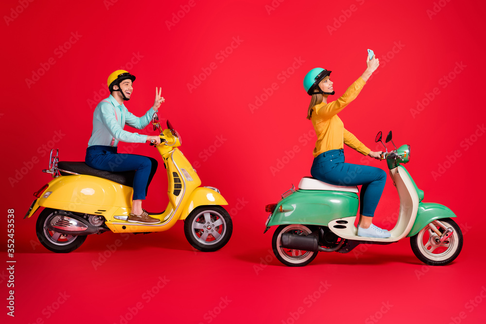 Profile side view of her she his he nice attractive cheerful friends friendship riding moped taking selfie showing v-sign having fun isolated on bright vivid shine vibrant red color background Profile side view of her she his he nice attractive cheerful friends friendship riding moped taking selfie showing v-sign having fun isolated on bright vivid shine vibrant red color background