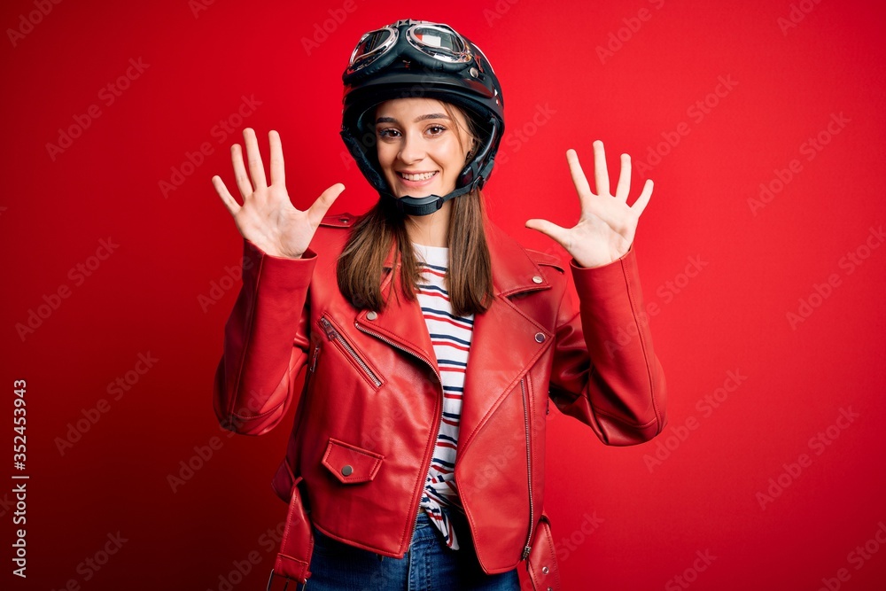 Young beautiful brunette motocyclist woman wearing motorcycle helmet and red jacket showing and pointing up with fingers number ten while smiling confident and happy. Young beautiful brunette motocyclist woman wearing motorcycle helmet and red jacket showing and pointing up with fingers number ten while smiling confident and happy.