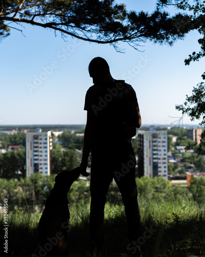silhouette of a guy and a dog standing on a slope above the city