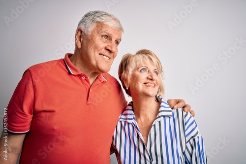 Senior beautiful couple standing together over isolated white background looking away to side with smile on face, natural expression. Laughing confident.