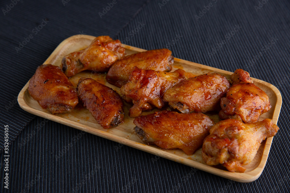 Baked chicken wings in a wooden dish on a dark cloth.