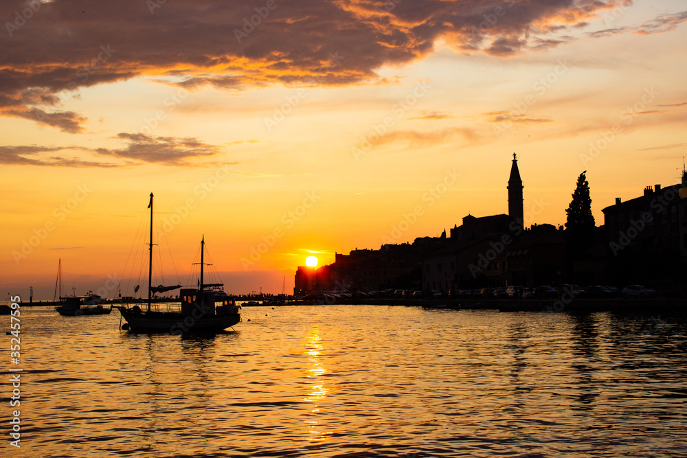Adriatic sea with some boats sailing and the view of the croatian houses of Rovinj, Croatia, and the bell tower of the Church of St Euphemia at the background, during the sunset