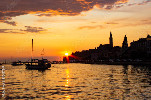 Sunset in Rovinj, Croatia, with a boat sailing in the Adriatic Sea and the sunrays reflected on the water, with the old town at the background © Jesus Barroso