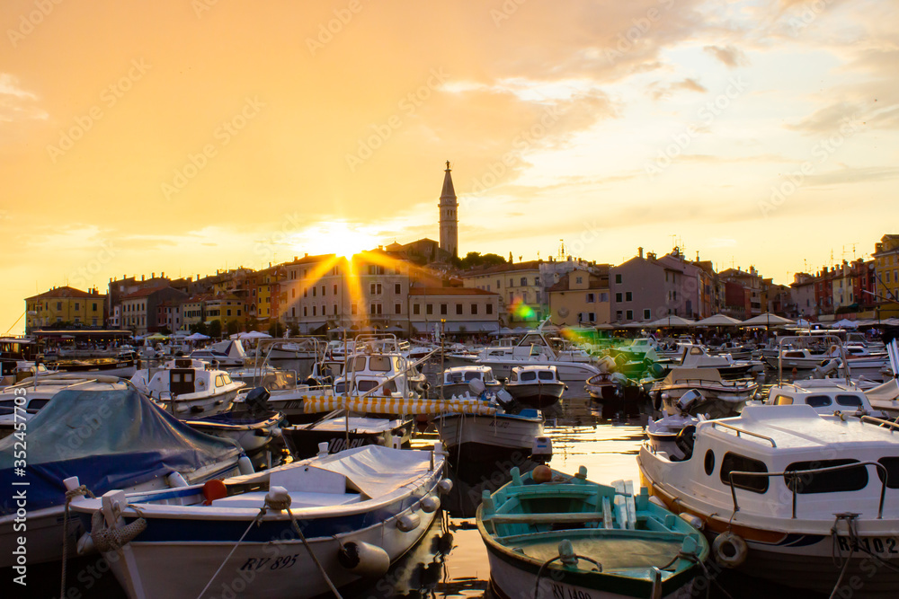 Rovinj, Croatia; 7/18/2019: Port of Rovinj, with many boats at the foreground and the view of the croatian houses and the bell tower of the Church of St Euphemia at the background, during the sunset