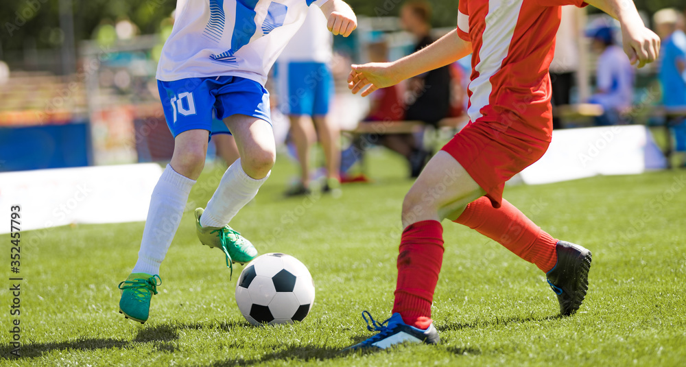 Two junior level soccer players running and kicking a soccer ball. Male footballers in dribbling duel during tournament match Two junior level soccer players running and kicking a soccer ball. Male footballers in dribbling duel during tournament match