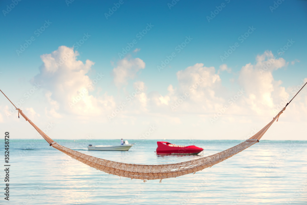 Empty hammock under tall palm trees on tropical beach - obrazy, fototapety, plakaty 