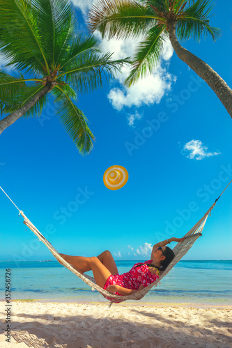 Young girl resting in a hammock under tall palm trees, tropical beach