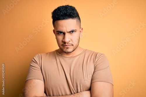 Young handsome man wearing casual t-shirt standing over isolated yellow background skeptic and nervous, disapproving expression on face with crossed arms. Negative person.