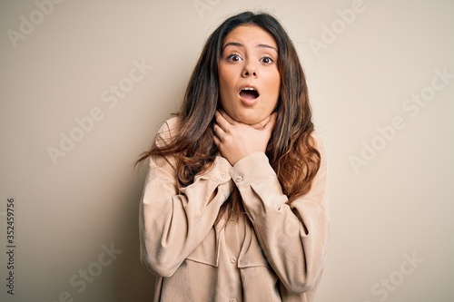 Young beautiful brunette woman wearing casual shirt standing over white background shouting and suffocate because painful strangle. Health problem. Asphyxiate and suicide concept.