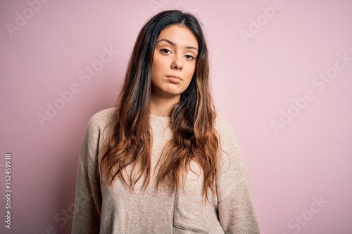 Young beautiful brunette woman wearing casual sweater standing over pink background looking sleepy and tired, exhausted for fatigue and hangover, lazy eyes in the morning.