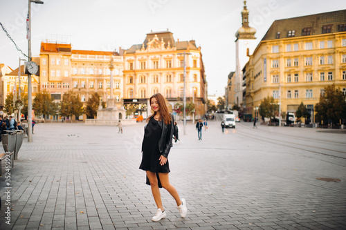 A young beautiful stylish girl in a black summer dress and jacket and with a purse walks through the old city.Girl-model in the Czech Republic. BRNO