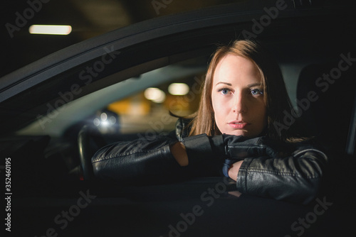 A young woman driver is looking through the car window at night.