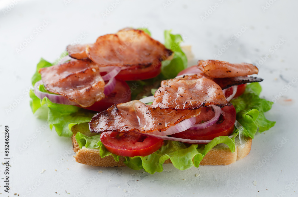 Grilled bacon sandwich with salad, tomato and onion on a white table Grilled bacon sandwich with salad, tomato and onion on a white table