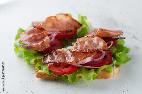 Grilled bacon sandwich with salad, tomato and onion on a white table