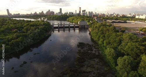 4K cloudy afternoon aerial scenic footage of hydro system dam regulating Moscow River water levels overlooking green park, distant city sky scrapers in Krylatskoye area in Moscow, Russia photo