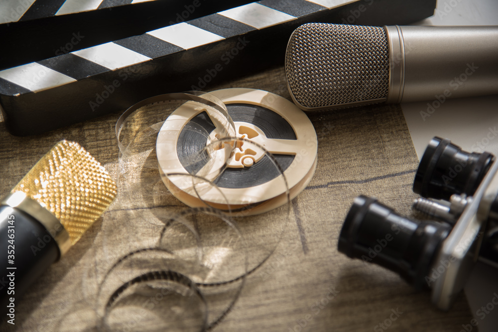 Fototapeta premium Film reel, movie clapperboard, two microphones and an old movie camera with two lenses on a table with a gray