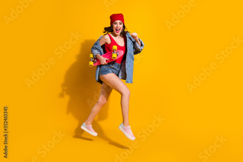 Full length photo of energetic excited cheerful girl youth student jump run to sporty skateboard training wear denim read hedwear singlet sneakers isolated over bright color background