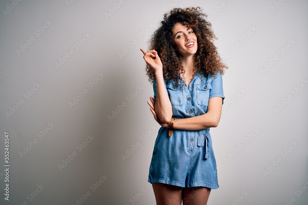 Young beautiful woman with curly hair and piercing wearing casual denim dress with a big smile on face, pointing with hand and finger to the side looking at the camera. Young beautiful woman with curly hair and piercing wearing casual denim dress with a big smile on face, pointing with hand and finger to the side looking at the camera.