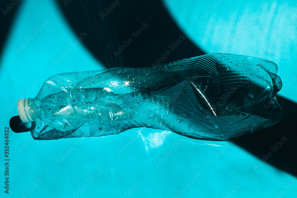 Crumpled empty plastic PVC bottle on a blue background. The concept of plastic pollution. Disposable plastic is a human addiction that destroys our planet and affects our waters, marine life Crumpled empty plastic PVC bottle on a blue background. The concept of plastic pollution. Disposable plastic is a human addiction that destroys our planet and affects our waters, marine life