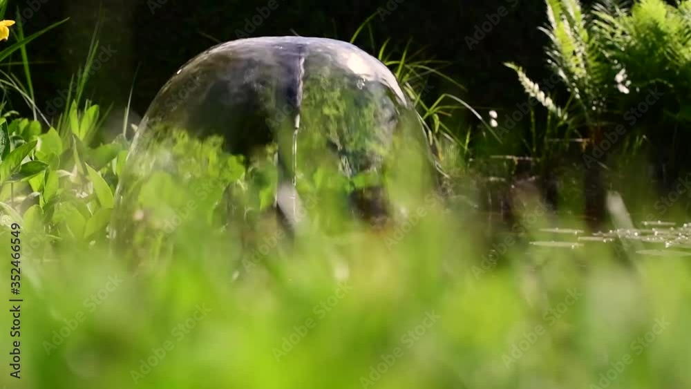 Plätscherndes Wasserspiel auf einem Gartenteich, grüne Uferbepflanzung-Beruhigender Hintergrund Plätscherndes Wasserspiel auf einem Gartenteich, grüne Uferbepflanzung-Beruhigender Hintergrund