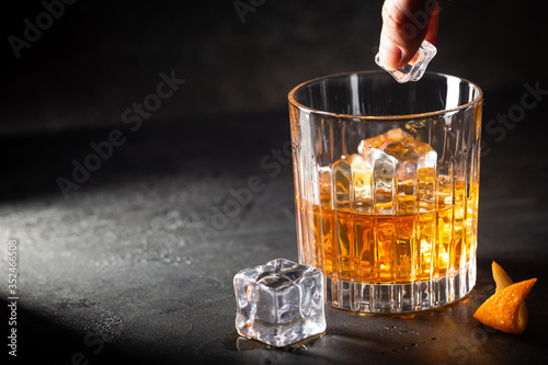 Glass of scotch whiskey with ice cubes on black background