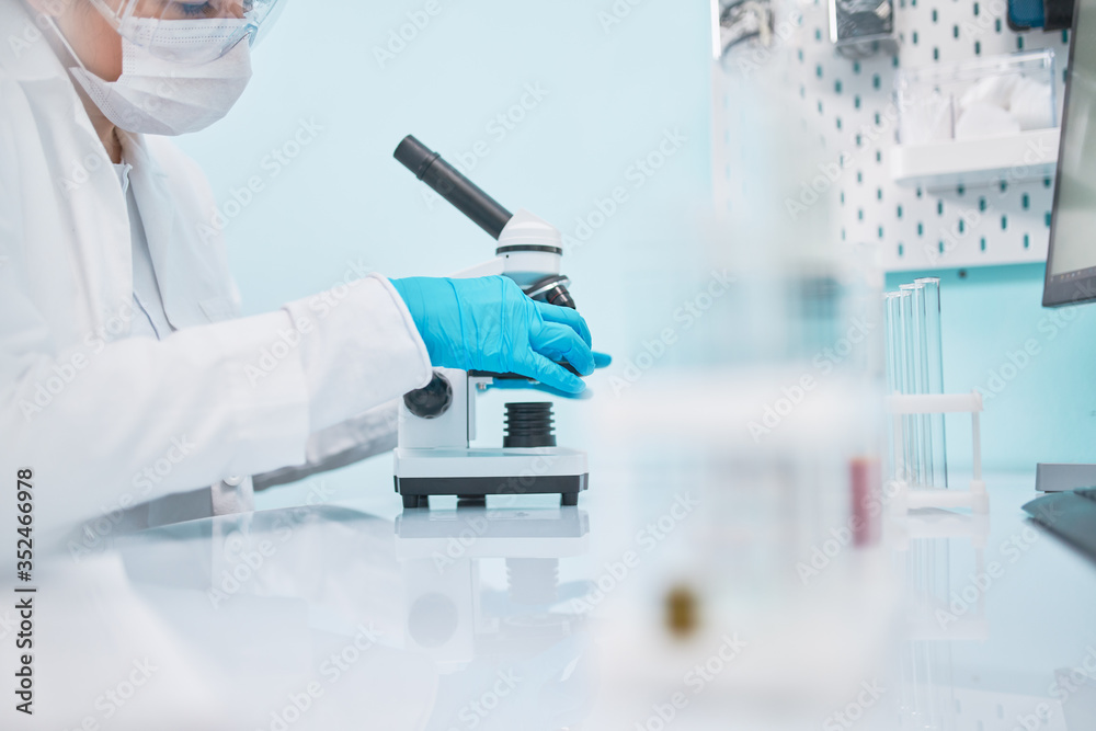 Female laboratory assistant in medical mask next to microscope Female laboratory assistant in medical mask next to microscope