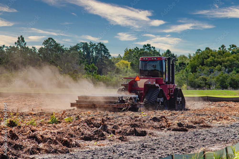 Fototapeta premium A piece of construction equipment drags a heavy bladed-roller across a field to pulverize and compact recently cleared vegetation.