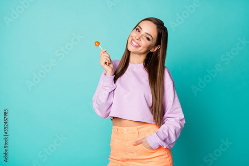 Photo of cute pretty funny lady hold lollipop candy on stick hands good mood sweets addicted person wear cropped pullover orange skirt isolated teal color background