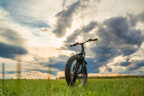 A Bicycle with thick wheels on a green meadow against a beautiful sky.