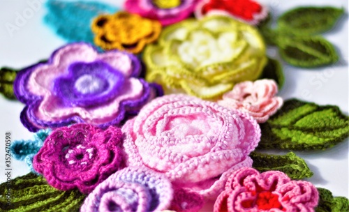 Multicolored crochet flowers and leaves image close up with bokeh background. 